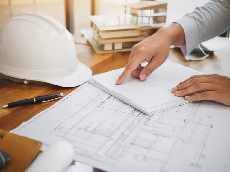 Documentos e planta técnica sobre a mesa ao lado de capacete de obra